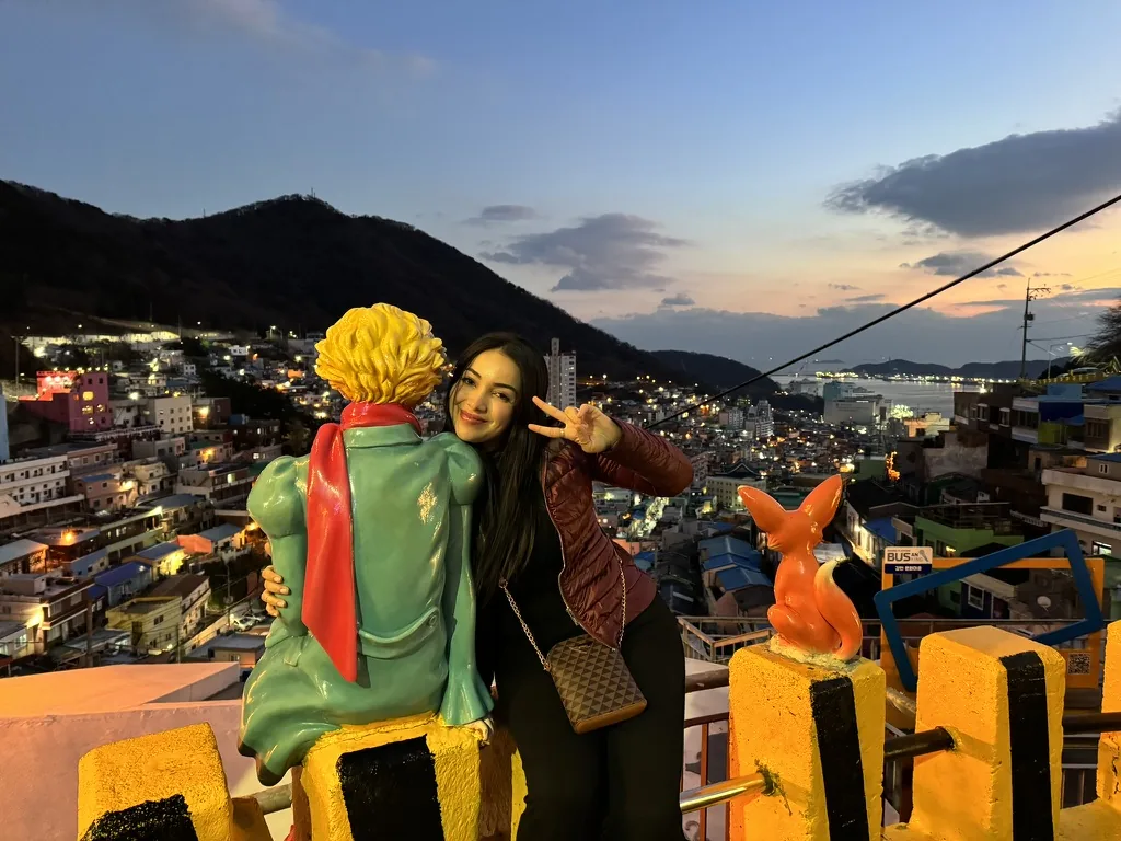 Viviane ao lado da estátua do Pequeno Príncipe na vila Gamcheon, ao entardecer