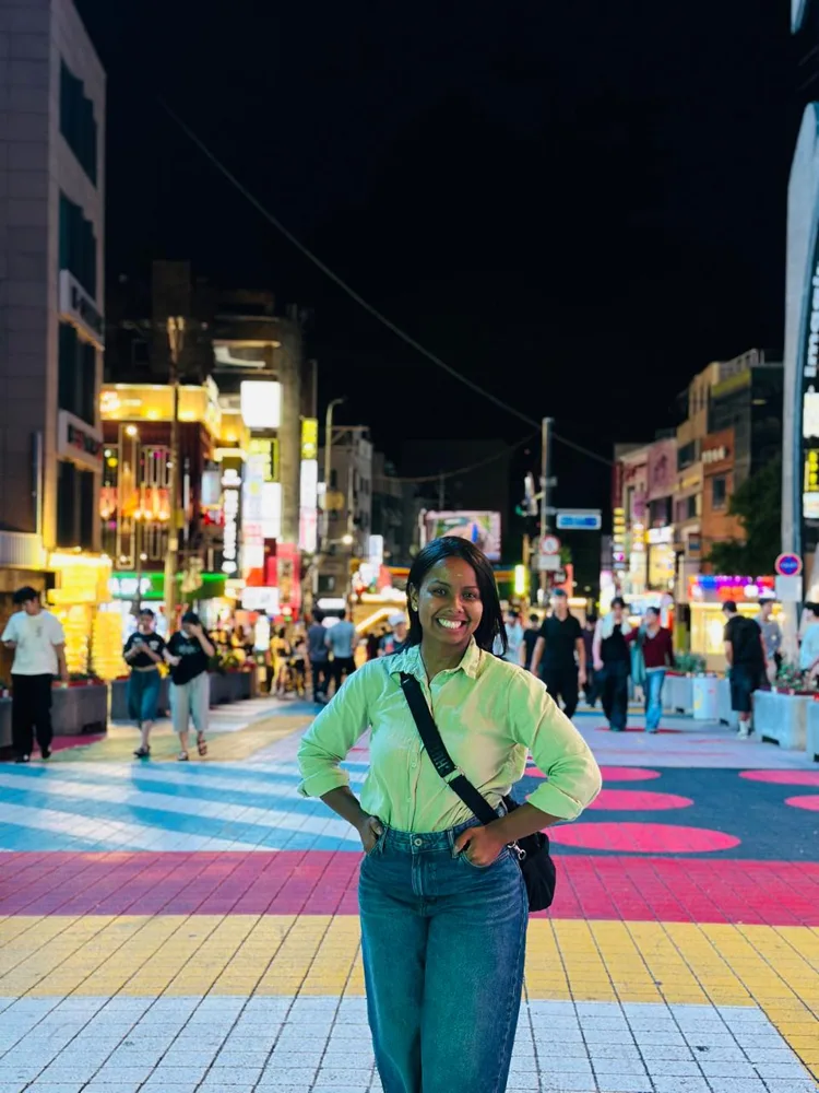 Viajante sorrindo numa rua de pedestres colorida de Hongdae, com letreiros acesos à noite