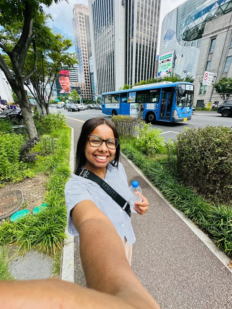 Selfie numa calçada arborizada do centro de Seul, com um ônibus azul passando atrás