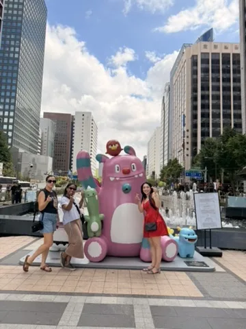 Três amigas posando numa praça do centro de Seul, ao lado de uma escultura rosa gigante