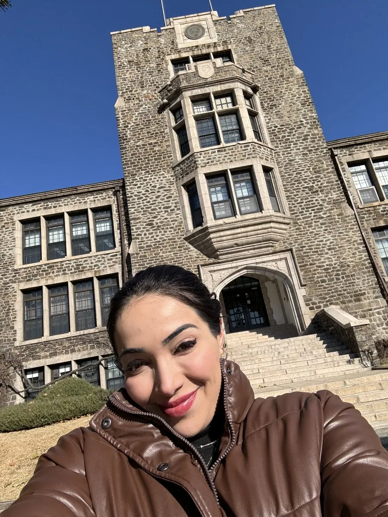 Viviane diante do prédio de pedra da escola de True Beauty