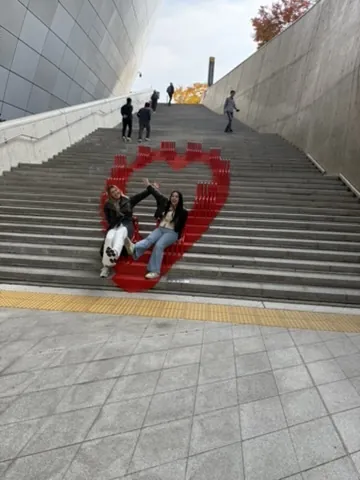 Duas amigas sentadas num coração vermelho pintado na escadaria do DDP