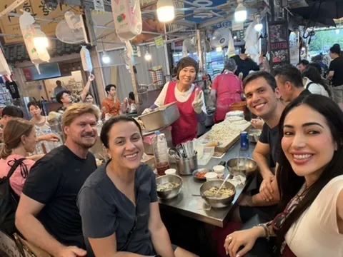 Grupo sentado no balcão de uma barraca do Gwangjang Market com a dona da barraca