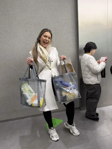 Viajante sorrindo com duas sacolas cheias de cosméticos coreanos