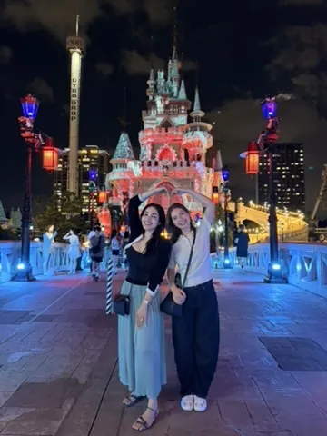 Duas amigas fazendo coração com os braços diante do castelo iluminado do Lotte World