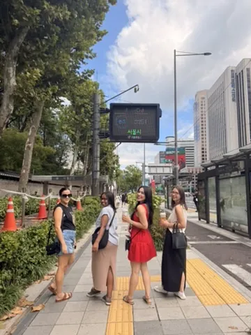 Quatro amigas caminhando juntas por uma calçada arborizada de Seul